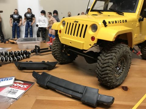 1989 Ford Bronco - A yellow Jeep Rubicon is shown with "Rubicon" text on its fender, surrounded by action figures and RC car parts.