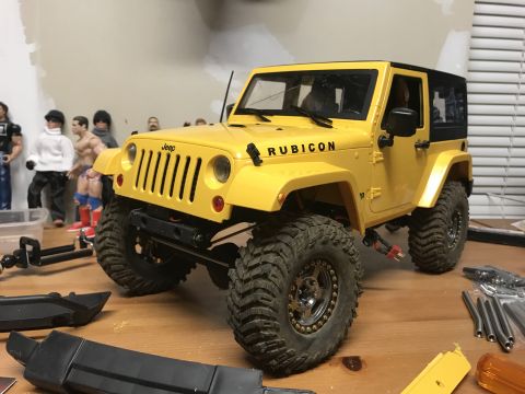 1989 Ford Bronco - A remote-controlled Jeep Wrangler Rubicon is shown on a table, with various toy figures and parts scattered around.