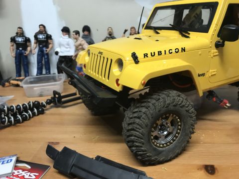 1989 Ford Bronco - A yellow Jeep Rubicon model sits on a wooden surface with action figures in the background.