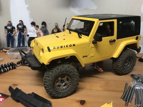 1989 Ford Bronco - A yellow Jeep Rubicon model sits on a wooden surface, surrounded by toy figures and tools.