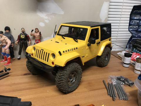 1989 Ford Bronco - A yellow Jeep Wrangler Rubicon model sits on a wooden surface, with action figures in the background.
