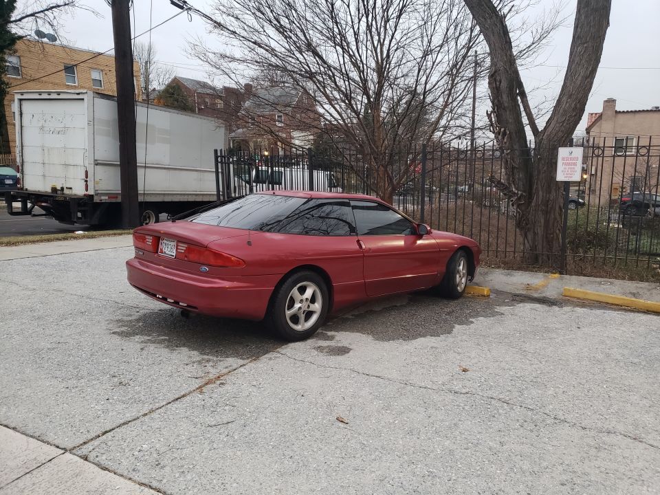 Red coupe parked on asphalt, rear-left quarter view. Tinted windows, aftermarket wheels