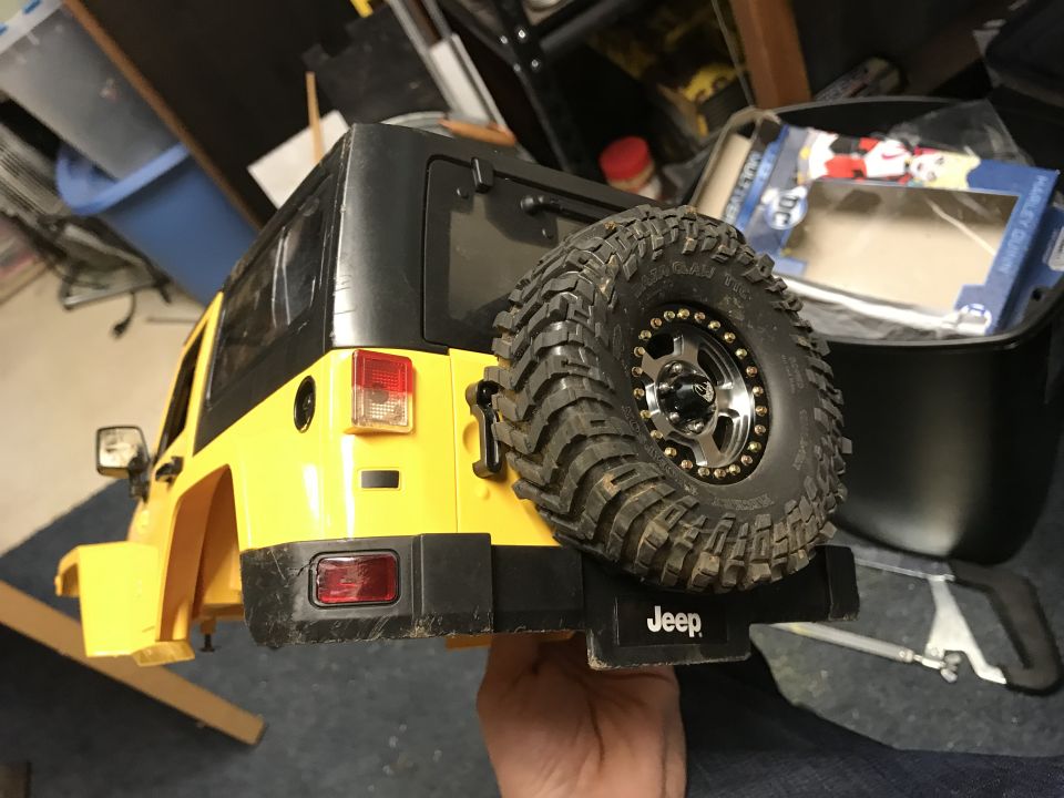 Yellow toy Jeep Wrangler with spare tire mounted on back, held by hand