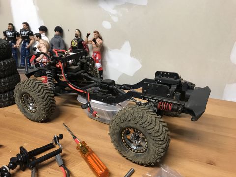 1989 Ford Bronco - RC crawler chassis with large tires and suspension components, surrounded by action figures and tools.