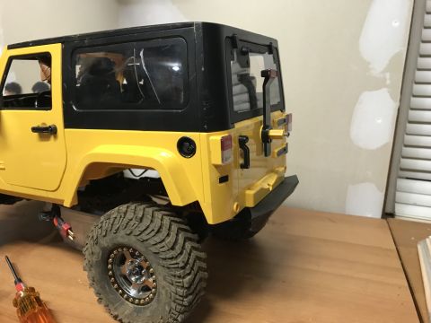 1989 Ford Bronco - A yellow remote-control Jeep Wrangler is shown from the rear, sitting on a wooden surface.