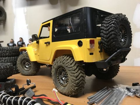 1989 Ford Bronco - A yellow Jeep Wrangler with a black hardtop and off-road tires is shown from a three-quarter rear view.