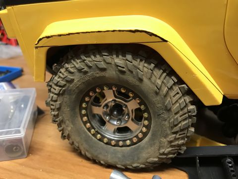 1989 Ford Bronco - Detail of an RC car's wheel well, showing a knobby tire and yellow bodywork with cut lines.