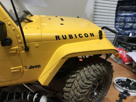 1989 Ford Bronco - Close-up view of a yellow Jeep Rubicon's hood and fender, highlighting the 'Rubicon' text and a large off-road tire.