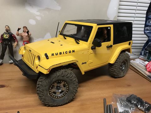 1989 Ford Bronco - RC Jeep Wrangler Rubicon model on a wooden surface with action figures in the background.