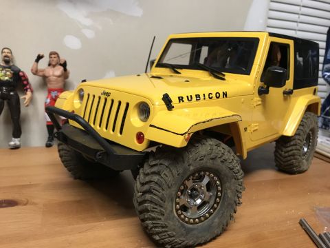 1989 Ford Bronco - A remote-controlled Jeep Wrangler Rubicon sits on a wooden surface, with action figures in the background.