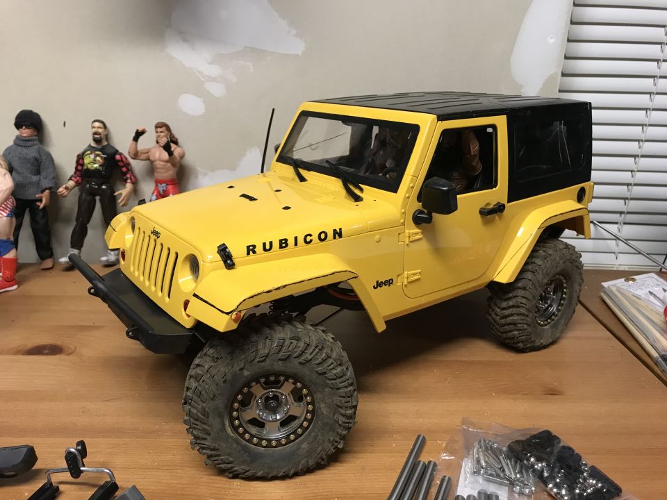 Yellow remote-control Jeep Wrangler Rubicon with black top and off-road tires on a wooden surface