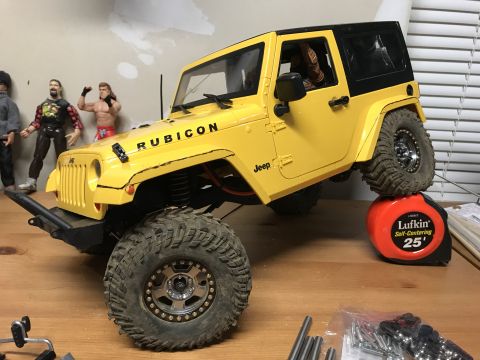 1989 Ford Bronco - A yellow toy Jeep Wrangler Rubicon is positioned on a tape measure, with action figures in the background.