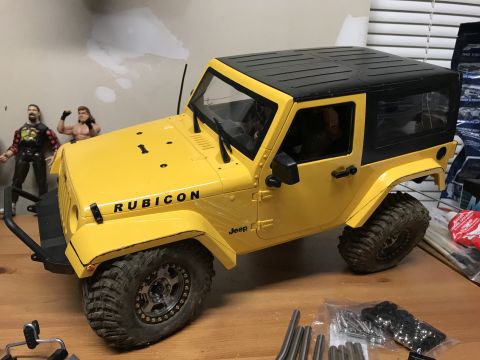 1989 Ford Bronco - A yellow Jeep Wrangler Rubicon model sits on a wooden surface, with other items in the background.