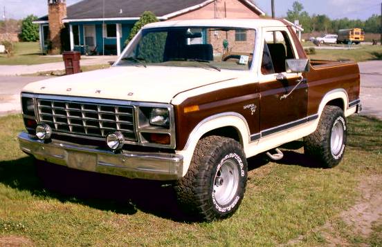 Two-tone brown and white 1980 Ford Bronco with aftermarket wheels and tires, parked on grass