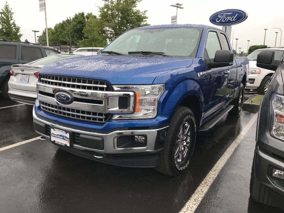 Blue 2018 Ford F-150 parked in a lot, front quarter view. Another truck is to the right