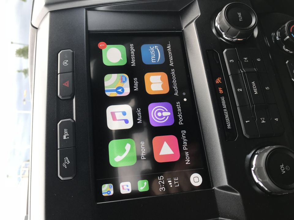 Car dashboard with infotainment screen displaying Apple CarPlay interface, showing apps like Messages, Maps, and Music