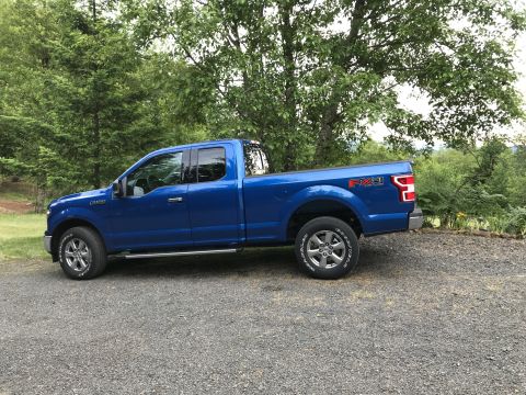 2018 Ford F-150 - A blue 2018 Ford F-150 pickup truck is parked on a gravel surface with trees in the background.