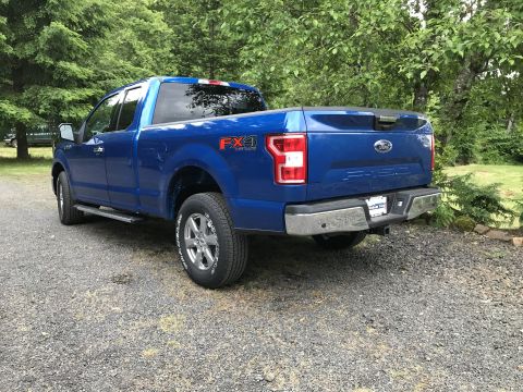 2018 Ford F-150 - A blue Ford F-150 pickup truck is parked on a gravel surface with trees and greenery surrounding it.