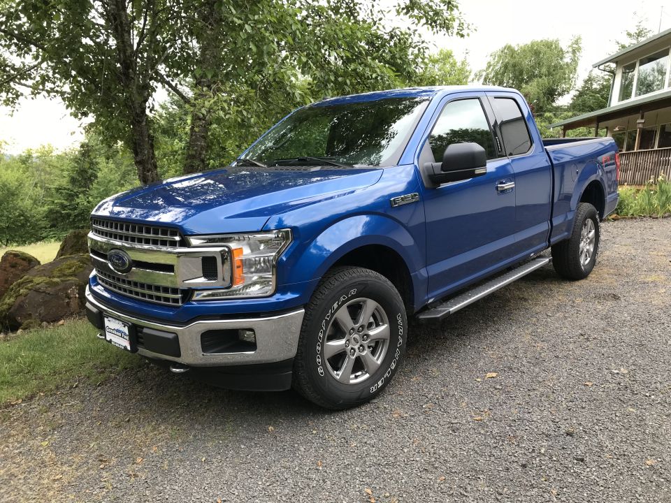 Blue 2018 Ford F-150 truck with chrome grille and running boards parked on gravel