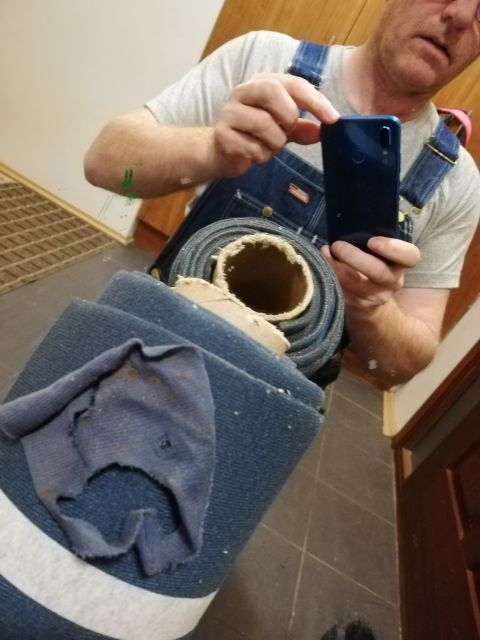 1996 Ford Bronco - Man in blue overalls and grey t-shirt holds a dark smartphone, reflected in a mirror.