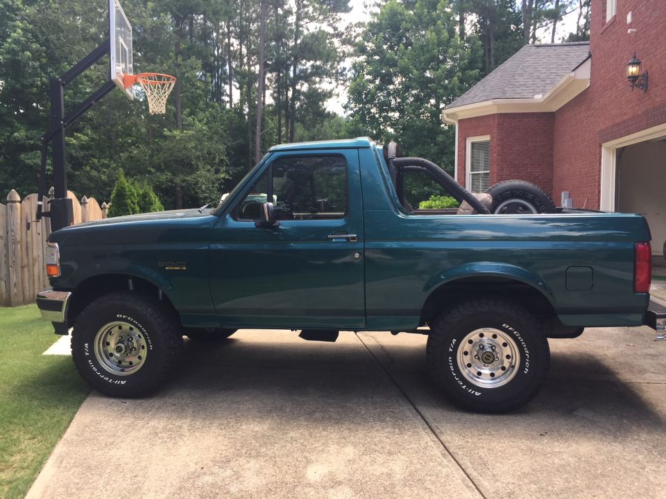 1996 Ford Bronco, side view, green paint, parked on concrete driveway next to a house