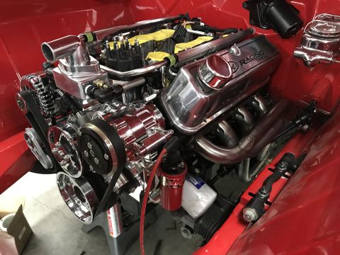 1964 Ford Fairlane - A highly polished chrome engine with racing valve covers and headers is installed in a red vehicle bay.