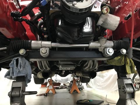 1964 Ford Fairlane - Underside view of a vehicle's engine and steering rack assembly, supported by jack stands, with exhaust headers visible.