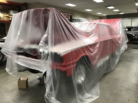 1964 Ford Fairlane - A red car is covered in plastic sheeting in a garage. Another classic car is visible in the background.
