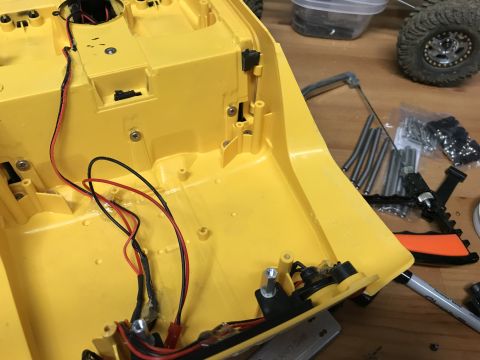 1989 Ford Bronco - A yellow plastic chassis with exposed wiring and various mechanical parts is laid out on a workbench.