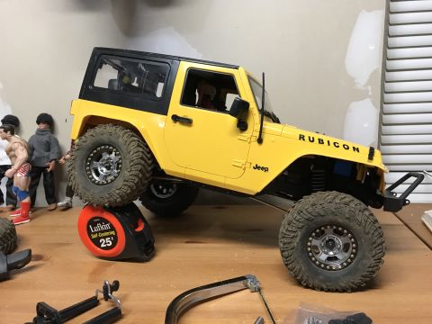 1989 Ford Bronco - A remote-controlled Jeep Wrangler is positioned on a workbench, with a tape measure supporting one of its wheels.