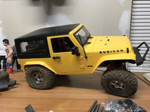 1989 Ford Bronco - A yellow Jeep Rubicon is parked on a wooden surface with some toy figures nearby.