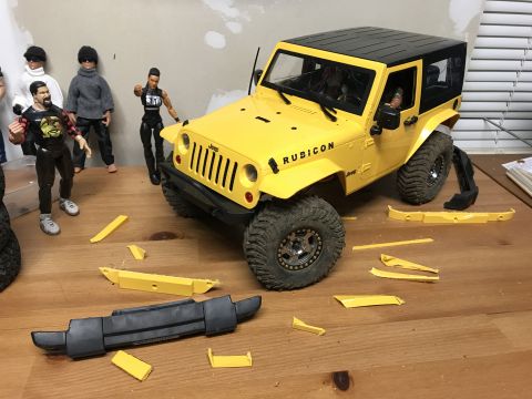 1989 Ford Bronco - A yellow toy Jeep Wrangler sits on a table with its bumper removed, surrounded by action figures and scattered plastic parts.