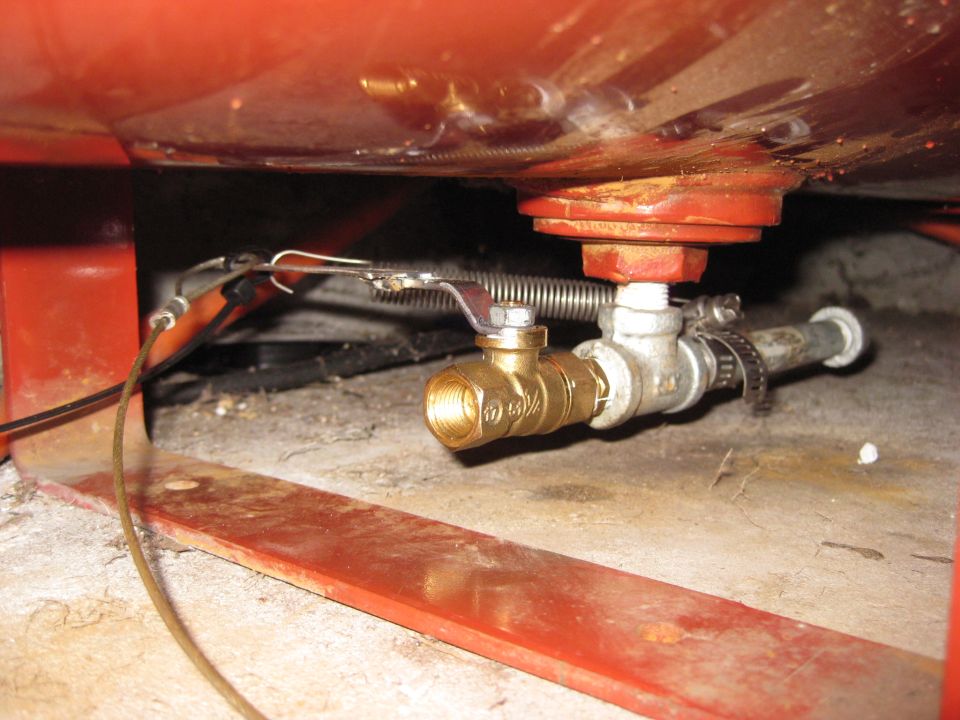 close-up of brass drain valve and metal pipe attached to red tank