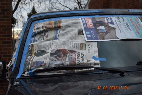 1996 Ford Bronco - The windshield of a vehicle is covered with newspaper and blue painter's tape, likely in preparation for a repair or painting.