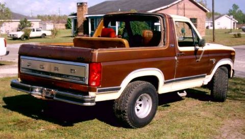 1980 Ford Bronco - A brown and white 1980 Ford Bronco is parked on a grassy lawn with houses in the background.