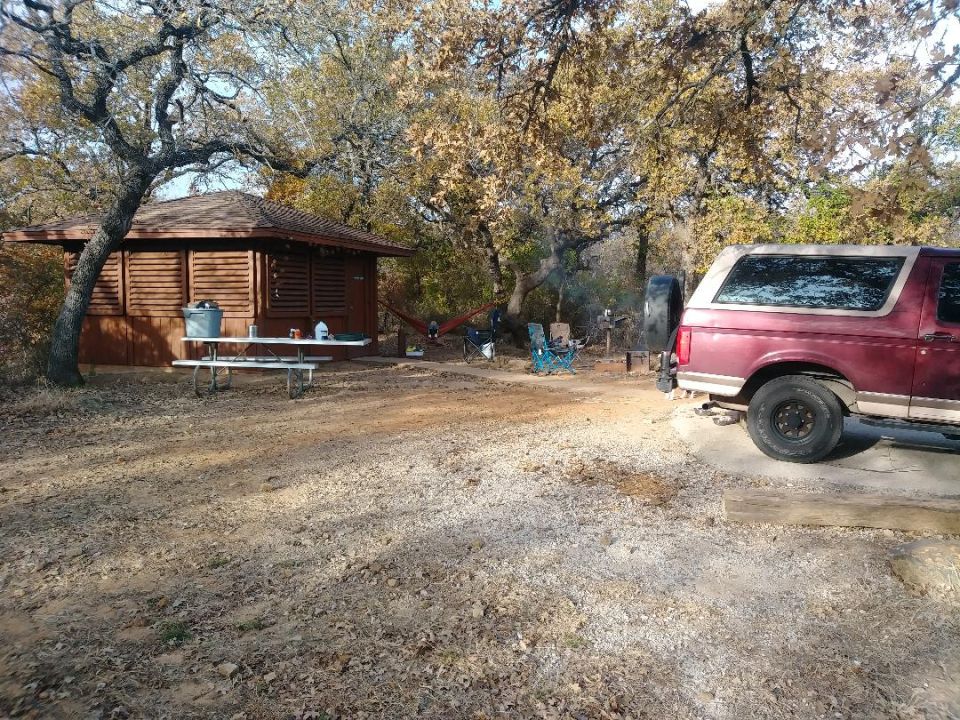 red Ford Bronco parked near a cabin with a campfire and chairs