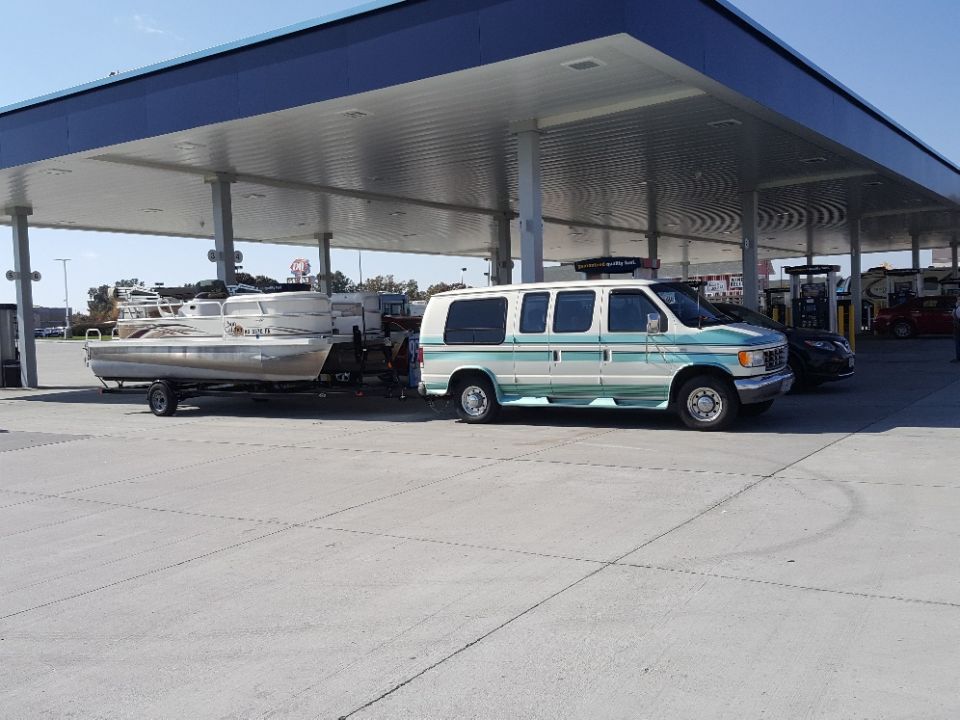 Teal and white van towing a pontoon boat at a gas station