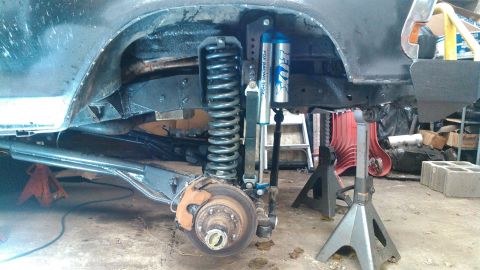 1978 Ford Bronco - Front suspension components and fender well of a vehicle undergoing repair, supported by jack stands.