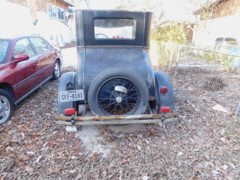 1909 Ford Model T - Rear view of a 1920s Ford Model T, showing its spare tire and Texas license plate. A red sedan is visible to the left.