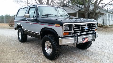 1986 Ford Bronco - This two-tone Ford Bronco features a prominent chrome grille and bumper, lifted suspension, and aftermarket wheels.