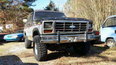 1986 Ford Bronco - This lifted Ford Bronco is parked in a lot with other vehicles under a clear sky.