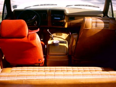 1980 Ford Bronco - The interior of the vehicle features distinct red and brown upholstery with a plaid pattern on the passenger seat.