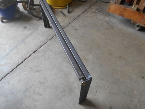 1992 Ford Bronco - Metal bracket with a hinge and bolt on a concrete floor, with shop equipment in the background.