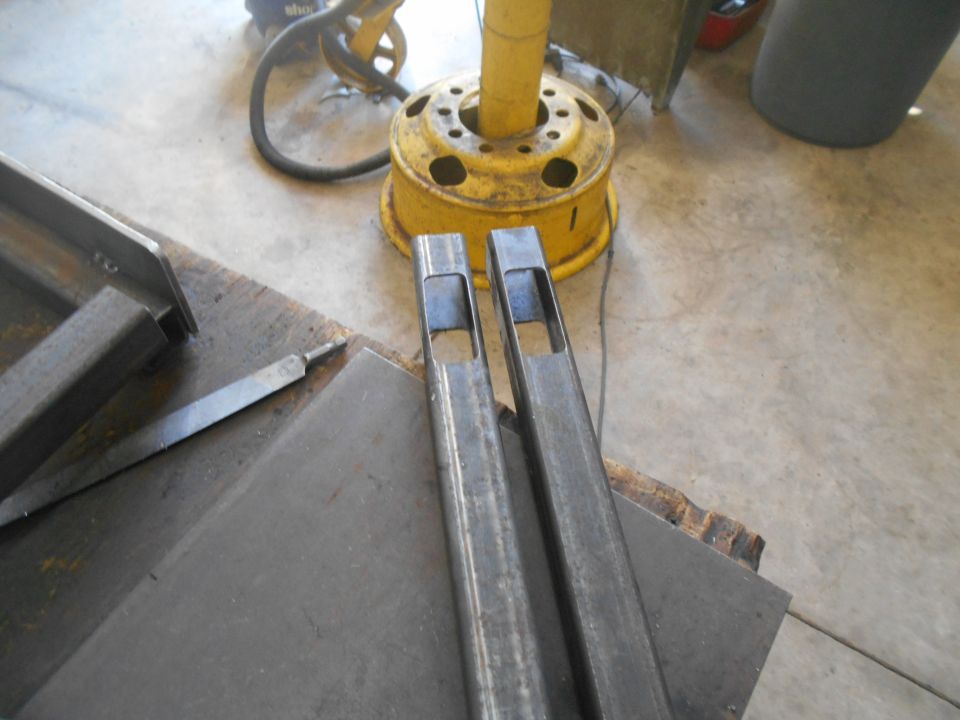 Two pieces of square metal tubing with rectangular cutouts, a file, and a yellow wheel rim on a concrete floor