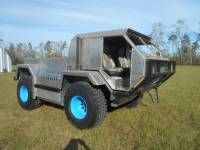 1992 Ford Bronco - A custom-built, silver, four-wheeled vehicle with large tires featuring bright blue rims sits parked on a grassy field under a partly cloud…
