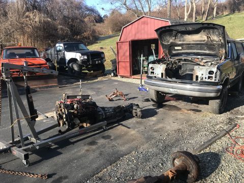 1992 Ford Bronco - A black Ford Bronco with its hood open is parked on a gravel driveway next to a red shed. An engine is suspended from an engine hoist in fr…