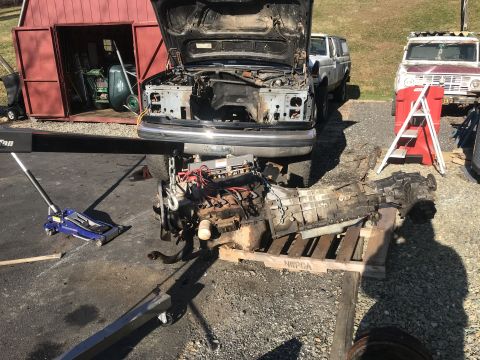 1992 Ford Bronco - An engine and transmission assembly is being removed from a vehicle using an engine hoist and supported by a blue hydraulic jack. The vehic…