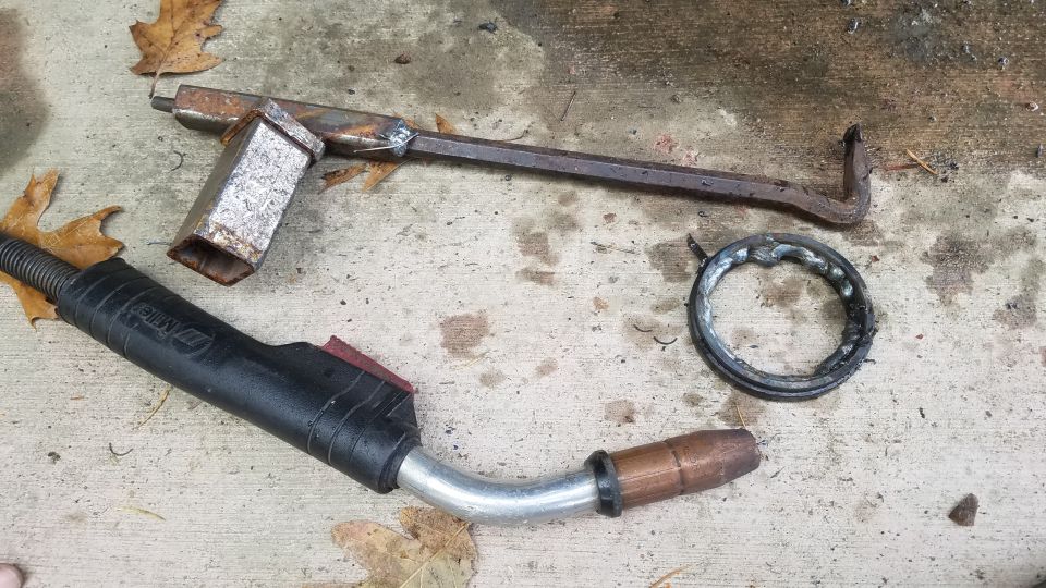 Welding torch, metal bar, and damaged metal ring on concrete.
