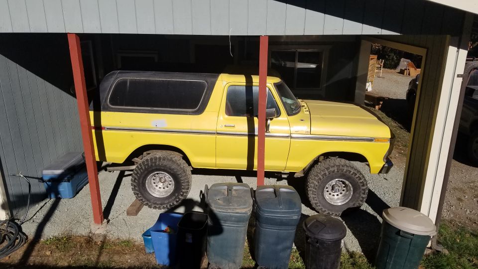 1978 Ford Bronco, yellow with black top, parked under cover on gravel
