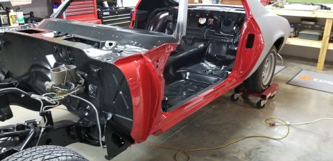 1970 Chevrolet Camaro - A partially restored red and gray Chevrolet Camaro is shown from a three-quarter front angle inside a garage. The interior floor and firewa…